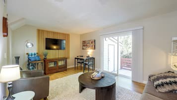 A living room with a flat-screen TV, a dining table with chairs, a sofa, a lamp, and a large window.