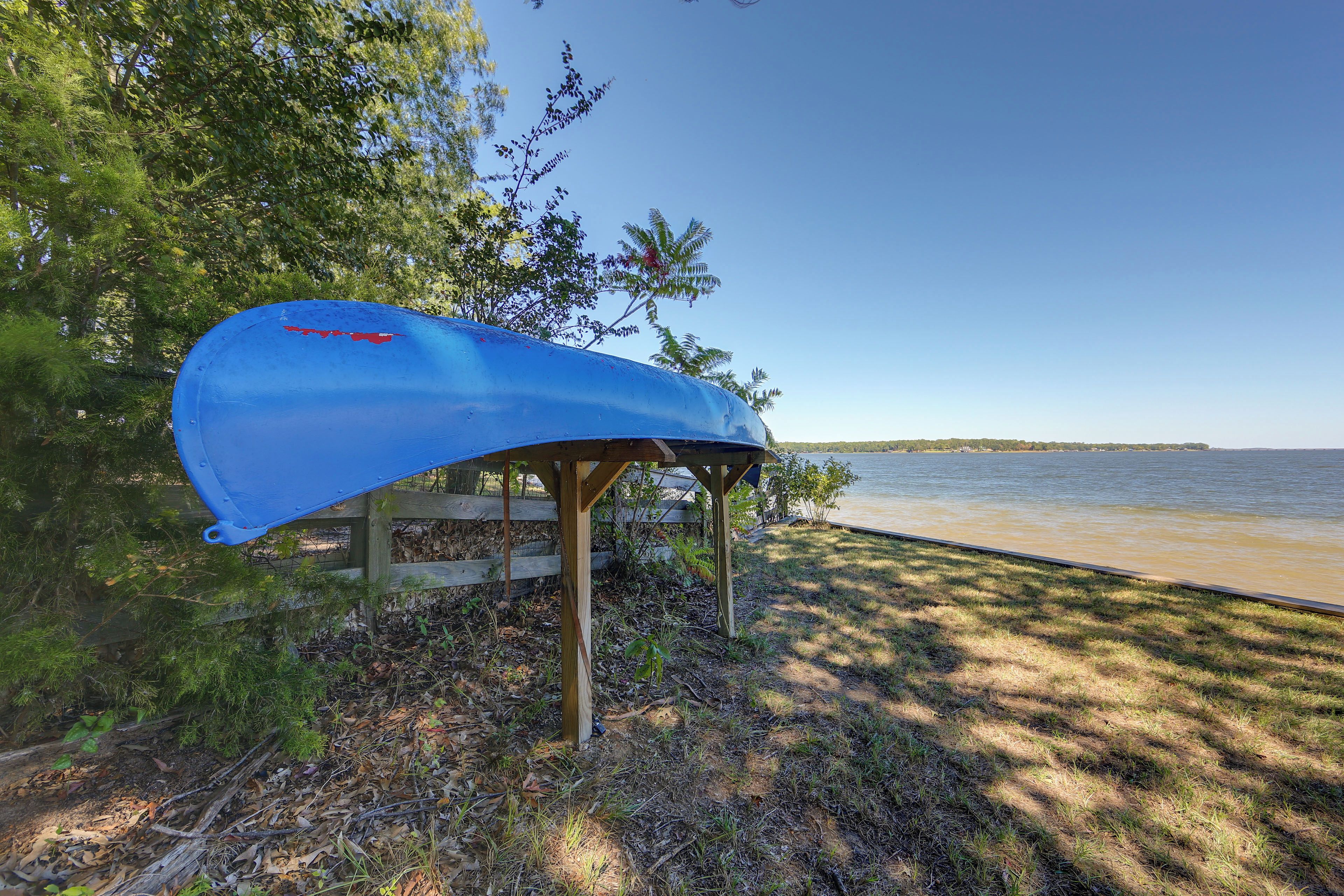 A blue kayak secured under a wooden structure by a lakeside.