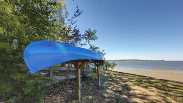 A blue kayak secured under a wooden structure by a lakeside.