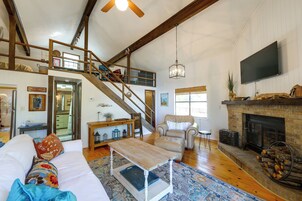 Un salón amplio con techo alto, chimenea, escalera que sube a un nivel superior y un televisor montado en la pared.