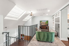 A modern interior with a staircase, a green upholstered bench, a television, and a bookshelf. - Historic Old Town Retreat Steps to King Street (Alexandria)