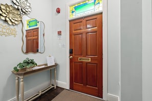 A wooden door with a brass handle, a mirror above it, and a welcome sign on a wooden console table with a plant. - Historic Old Town Retreat Steps to King Street (Alexandria)