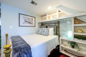 A bedroom with a bed, a bedside table with a lamp, a shelf with decorative items, and a framed picture on the wall. - Historic Old Town Retreat Steps to King Street (Alexandria)