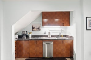A kitchen with wooden cabinets, a stainless steel dishwasher, a coffee maker, and a sink. - Historic Old Town Retreat Steps to King Street (Alexandria)