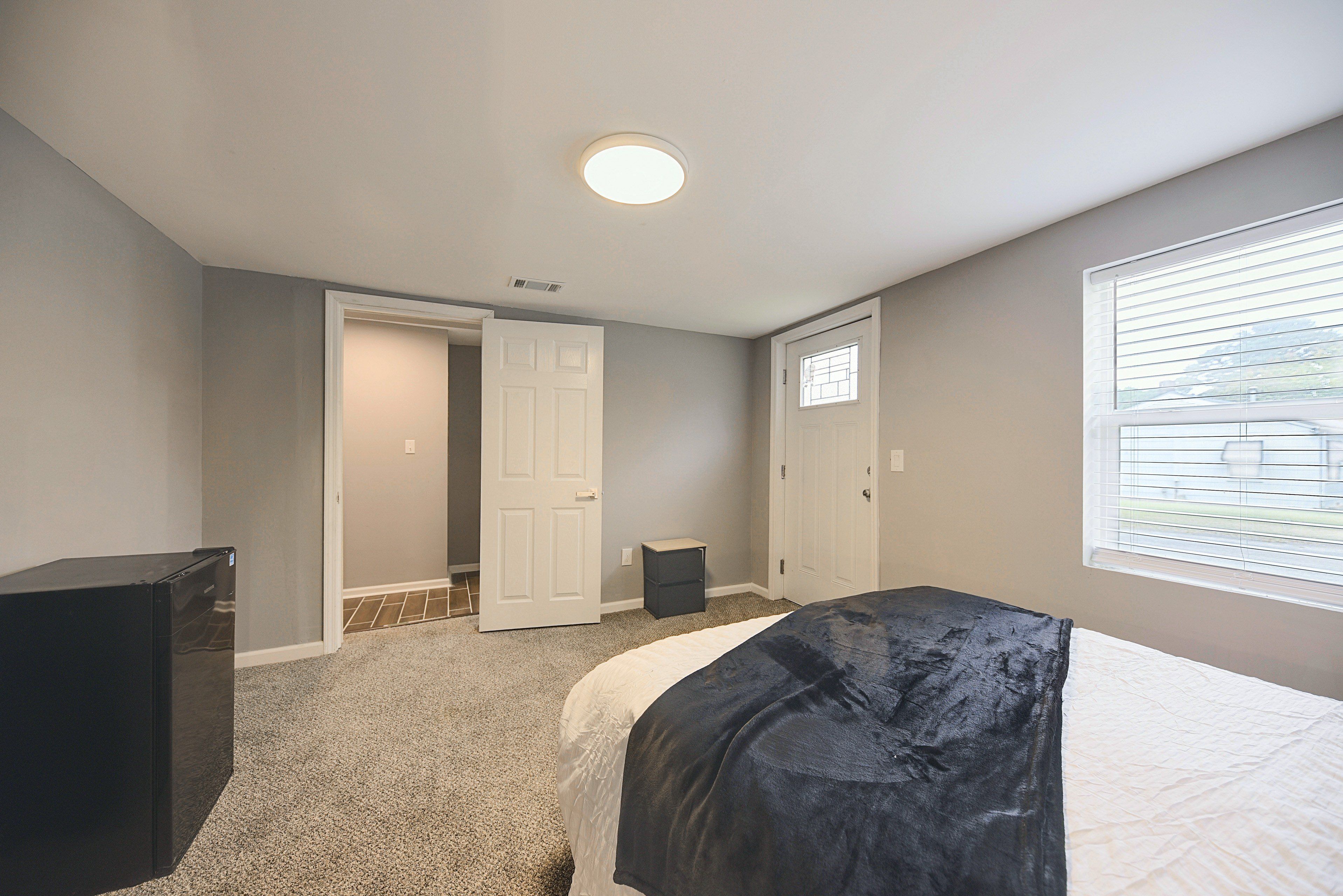 Un dormitorio con cama, cómoda, puerta y ventana con persianas.