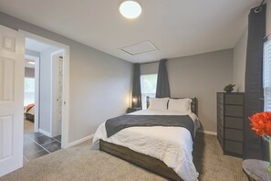 A bedroom with a bed, a dresser, a nightstand, and a window with curtains. - Hidden Orangeburg Gem! Spacious Modern Deco Ranch (Orangeburg)