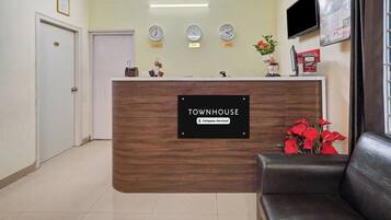 A reception desk with a sign indicating it is company-serviced. There are clocks above the desk showing different time zones, a television mounted on the wall, and a door labeled '101'.