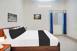 Un dormitorio con cama, mesita de noche, lámpara, un cuadro enmarcado de un tigre y un cuadro enmarcado de un paisaje, además de una ventana con cortinas.