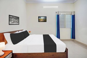 A bedroom with a bed, a nightstand, a lamp, a framed picture of a tiger, a framed landscape picture, and a window with curtains.