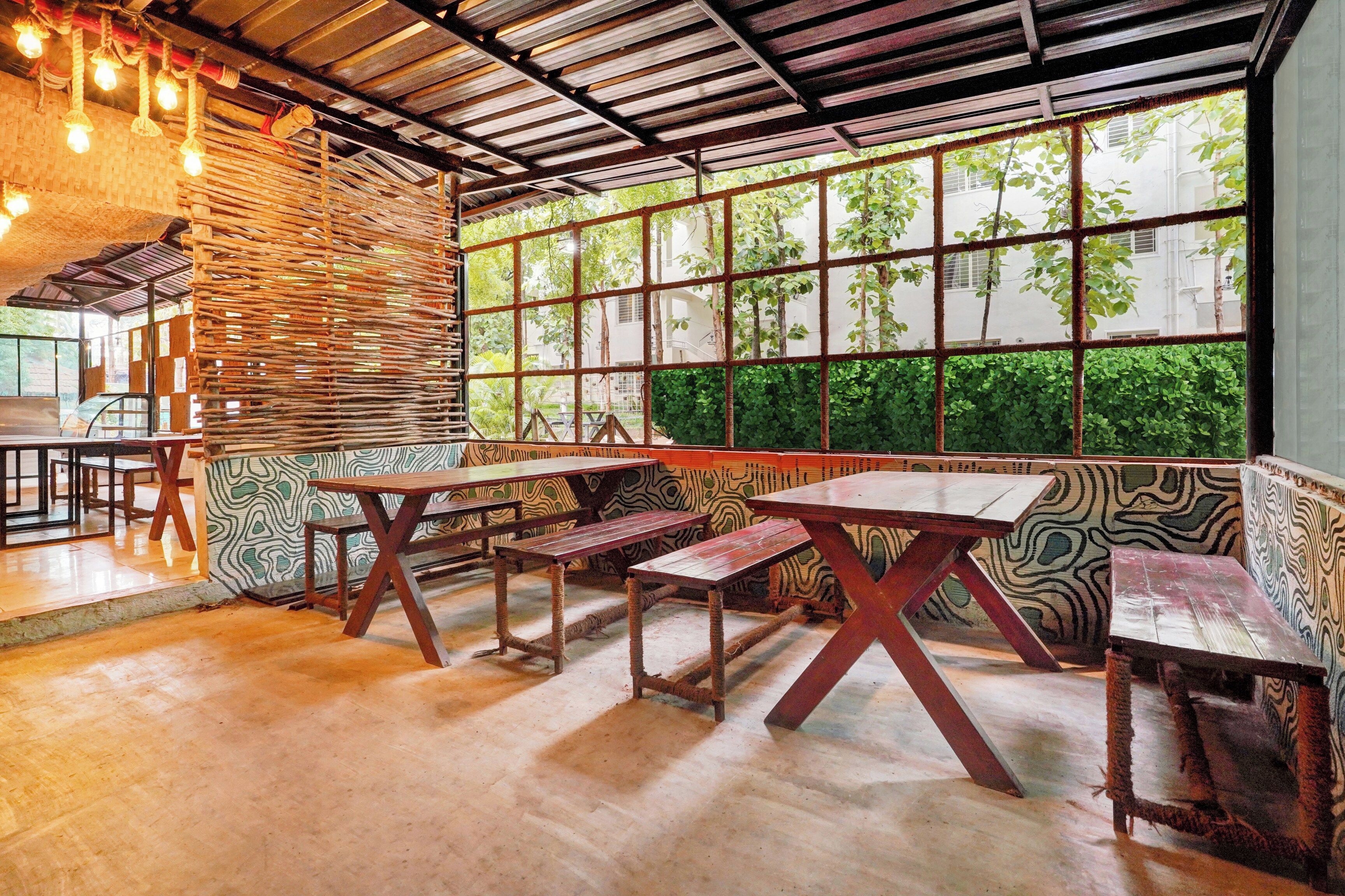 An indoor dining area with wooden tables and benches, a patterned wall, and large windows with a view of greenery.