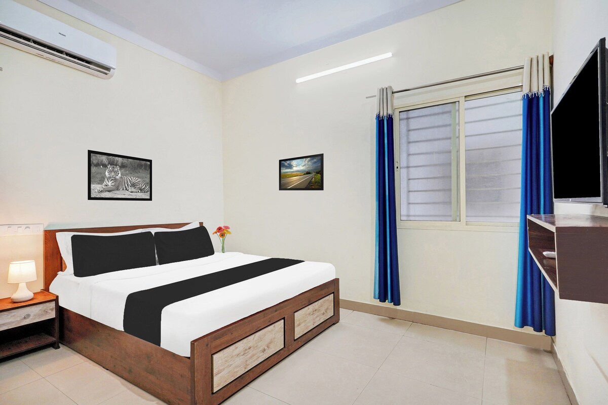 A hotel room with a bed, a nightstand, a lamp, a window with curtains, and two wall-mounted pictures.