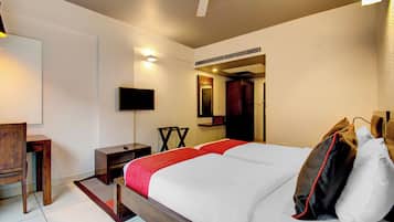 Una habitación de hotel con una cama, un escritorio, una silla, un televisor y un ventilador de techo.