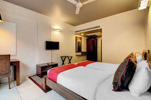 Una habitación de hotel con una cama, un escritorio, una silla, un televisor y un ventilador de techo.