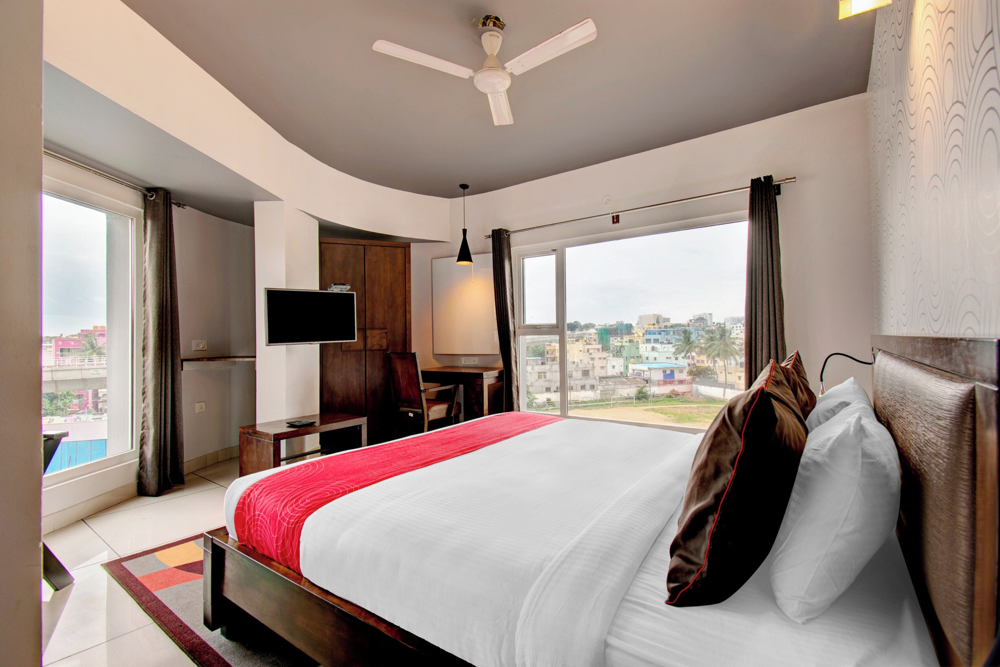 Habitación de hotel con cama, escritorio, silla, televisor y vista a la ciudad.