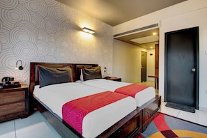 Habitación de hotel con una cama grande, dos mesitas de noche, una lámpara de pared y una puerta que da a otra habitación.