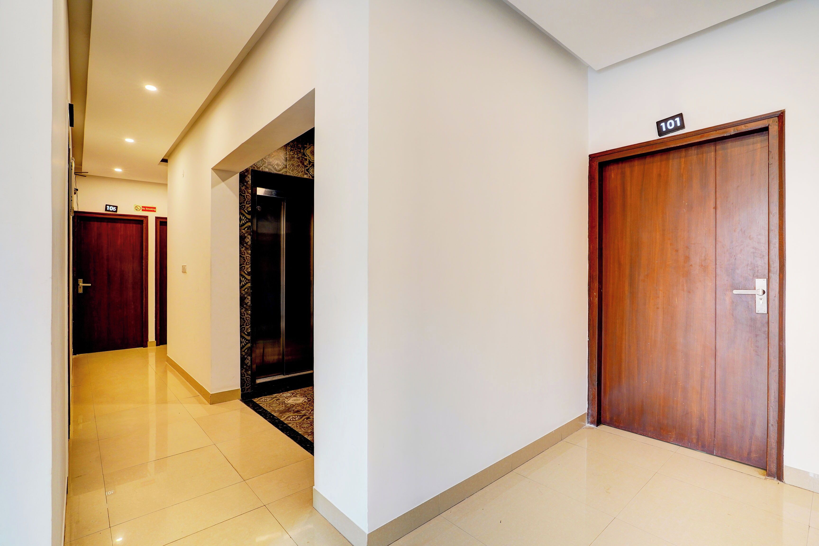 A hotel corridor with a wooden door marked '101', a 'No Smoking' sign, and a tiled floor.