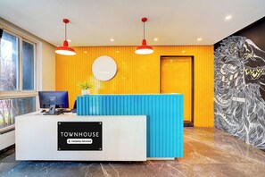 En reception med et skilt der viser 'Townhouse Company-Serviced' i en lys lobby med et stort vindue, en blå disk og en dekorativ vægdekoration.