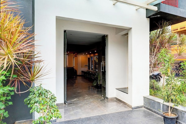 Una entrada de edificio moderno con puerta de vidrio, un pasillo que conduce al interior y varias plantas en macetas.