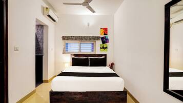 A hotel room with a bed, a ceiling fan, an air conditioning unit, a window with a view, and a mirror on the wall.