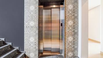 An elevator with a digital display, surrounded by patterned wall tiles and a marble staircase.