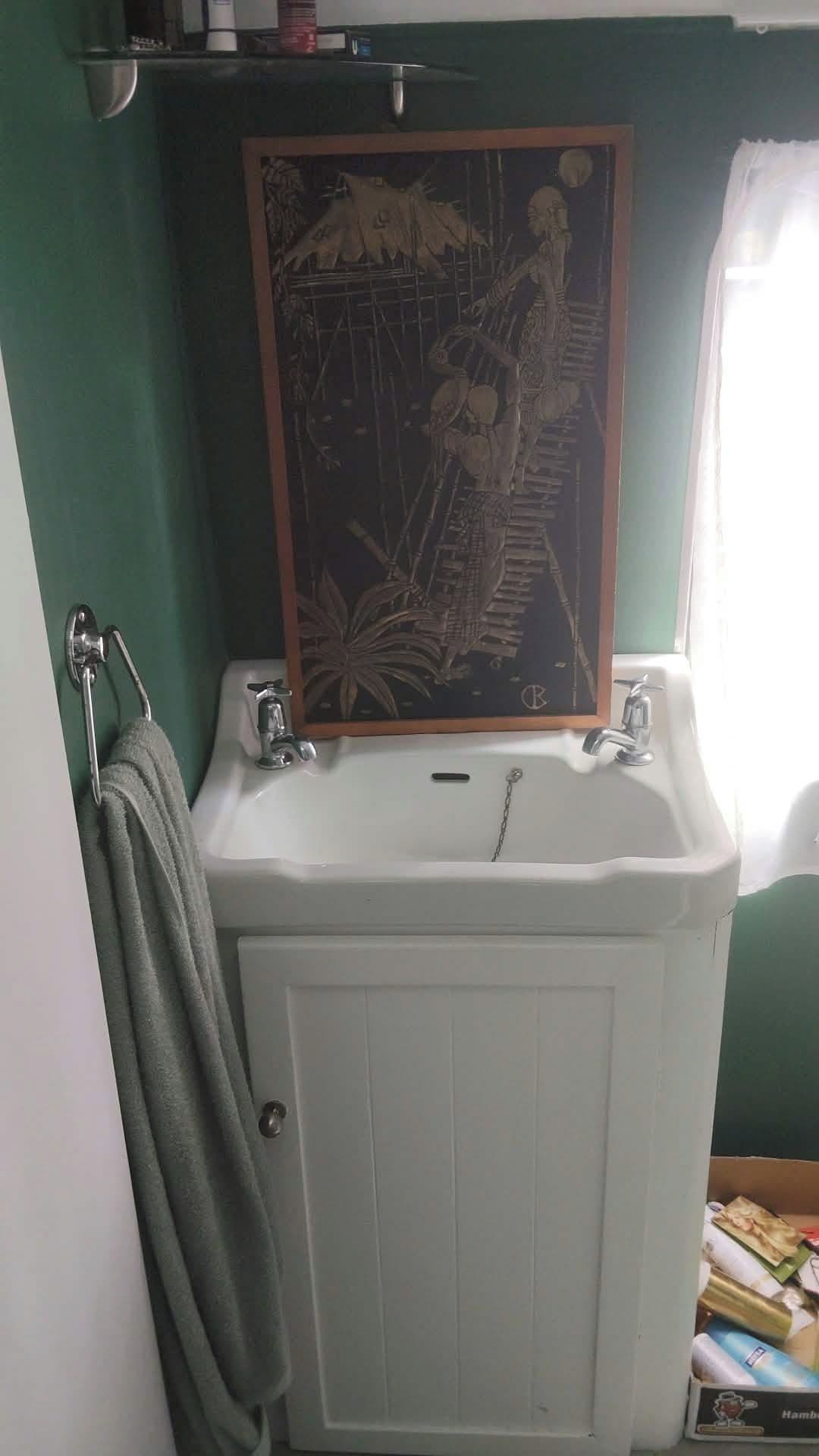 Ein Badezimmer mit einem weißen Waschbecken, einem Handtuchhalter und einem gerahmten Bild über dem Waschbecken.