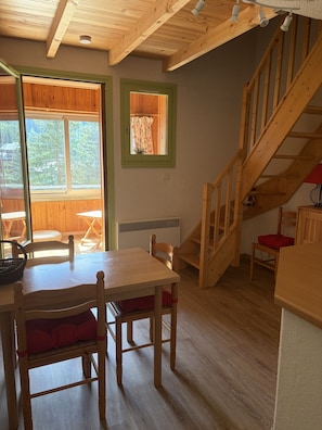 Ein Holzinnenraum mit einem Esstisch, Stühlen, einer Treppe und einem Fenster mit Vorhängen.