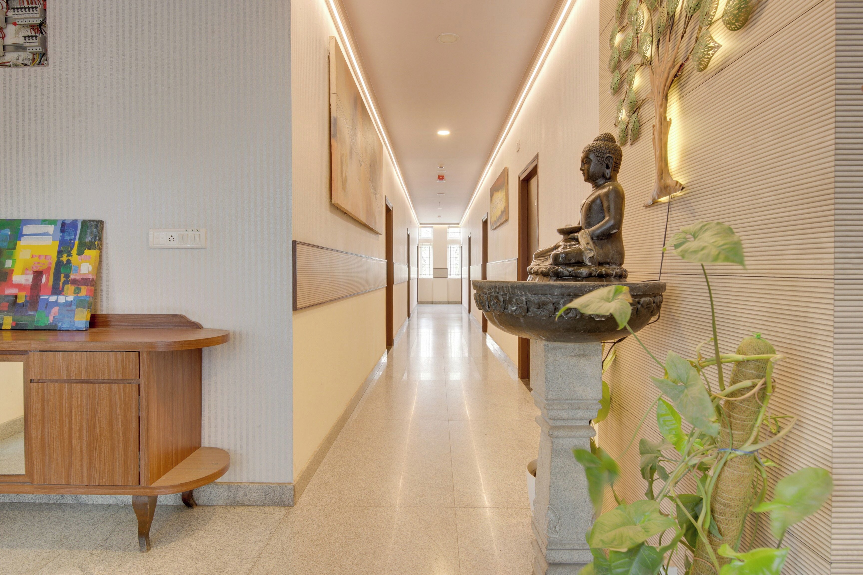 Un pasillo de hotel con una estatua, un cuadro colorido y una planta.