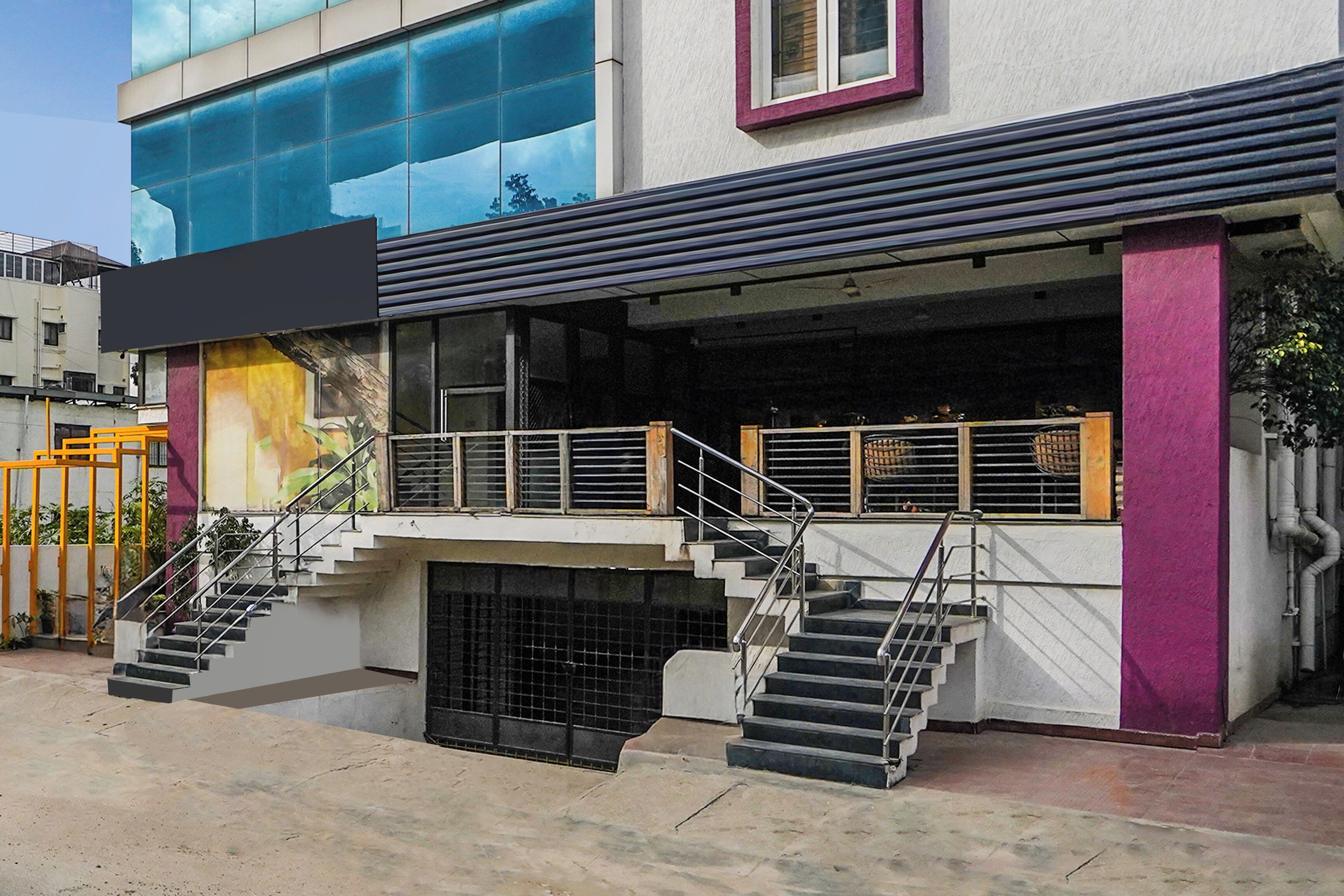 Un edificio de estilo arquitectónico moderno, con fachada de vidrio, una escalera que lleva a la entrada y un espacio exterior visible con barandilla de metal.