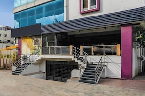 Un edificio de estilo arquitectónico moderno, con fachada de vidrio, una escalera que lleva a la entrada y un espacio exterior visible con barandilla de metal.