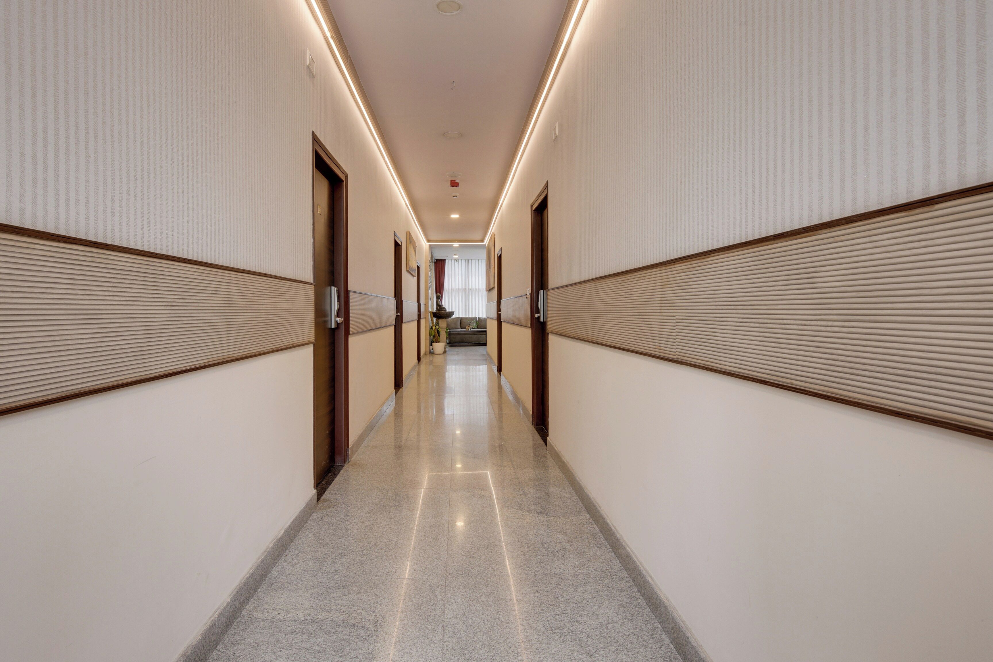 Un pasillo de hotel con piso pulido, paneles de madera en las paredes y puertas que dan a las habitaciones.