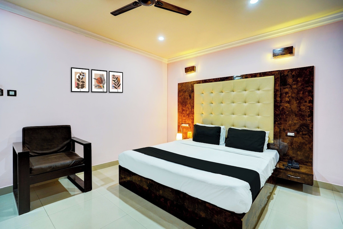 Quarto de hotel com uma cama grande, uma cadeira, ventoinha no teto e quadros nas paredes.