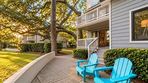 A two-story house with a balcony, a tree, and two blue chairs on a paved path. - Lakefront Villa - Kingston Beach Resort (Myrtle Beach)