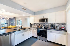 A modern kitchen with white cabinets, stainless steel appliances, and a black countertop. - Lakefront Villa - Kingston Beach Resort (Myrtle Beach)