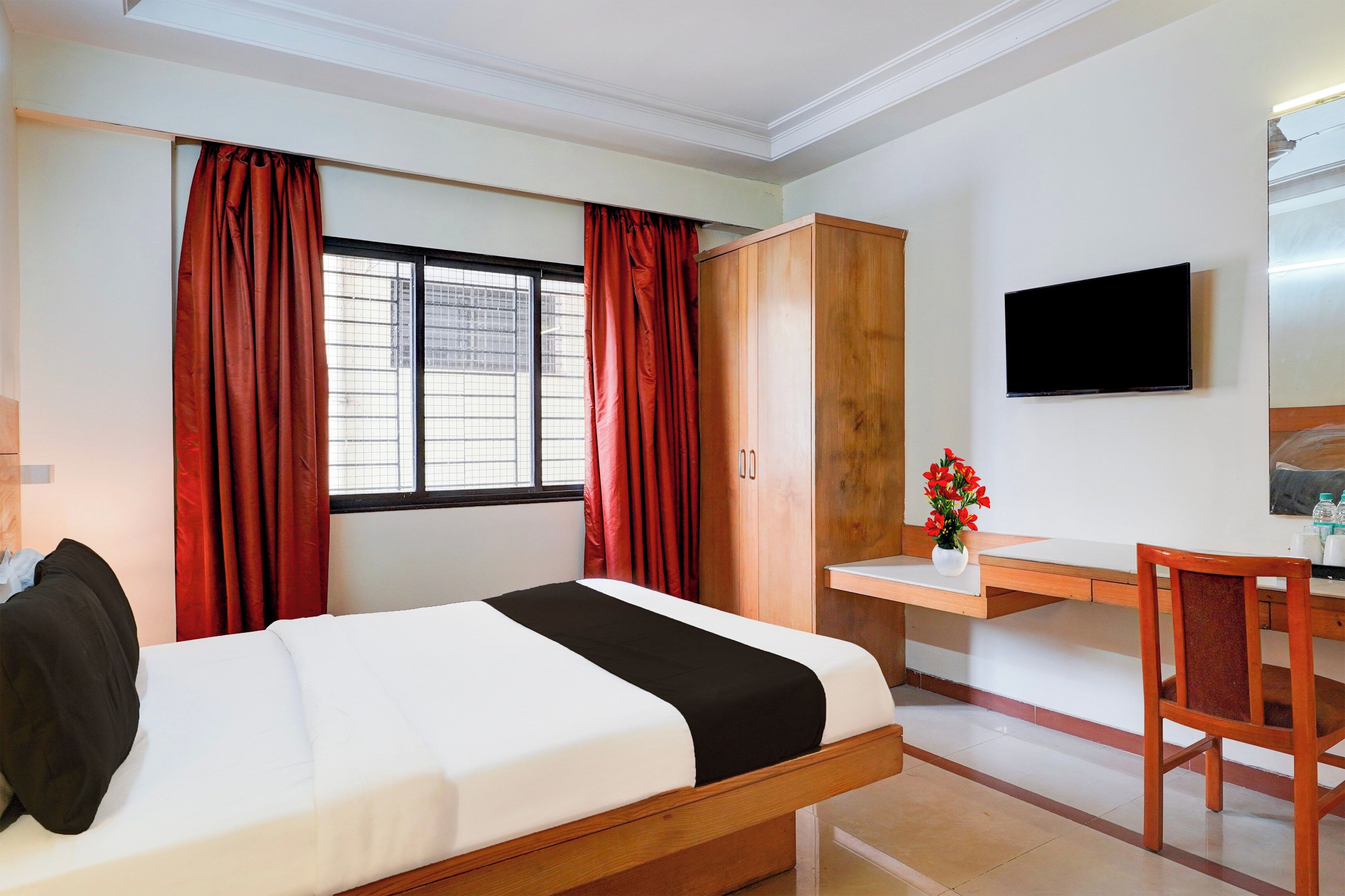 Une chambre d’hôtel avec un lit, un bureau, une chaise, une télévision et une fenêtre avec des rideaux.
