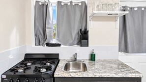 A kitchen with a gas stove, stainless steel sink, and a window with curtains. - Cozy Private Basement Unit Near DC & Metro (Glenarden)