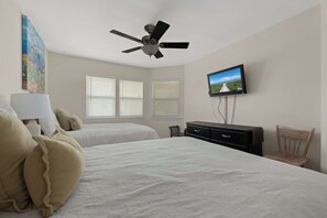 A bedroom with two beds, a ceiling fan, a TV, and a painting on the wall. - SPI Beach Access Condo - Pool, Game Room (South Padre Island)