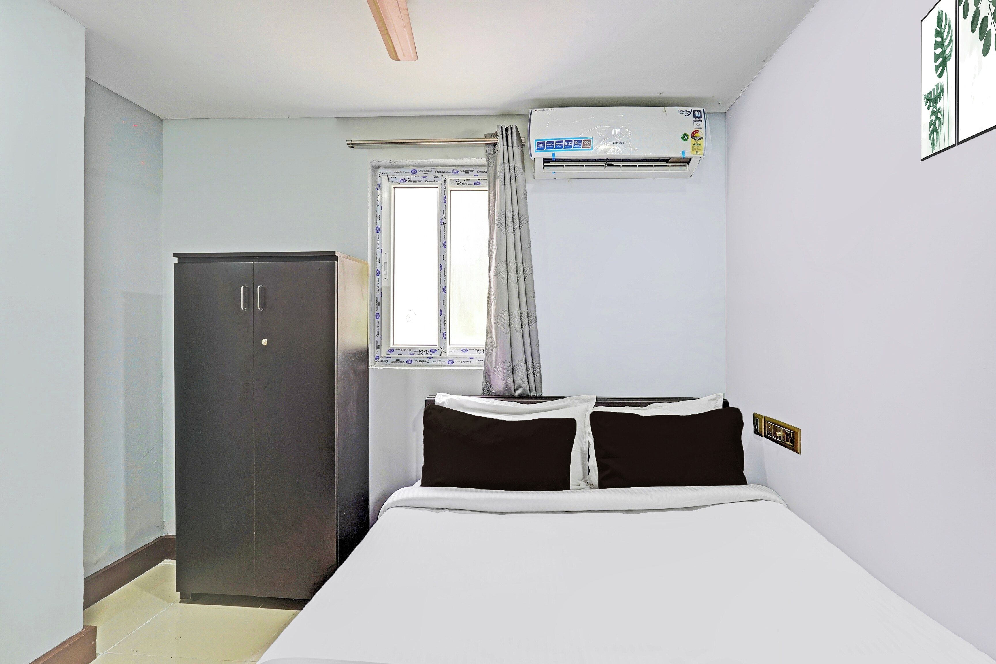A bedroom with a bed, a wardrobe, an air conditioning unit, and a window with curtains.
