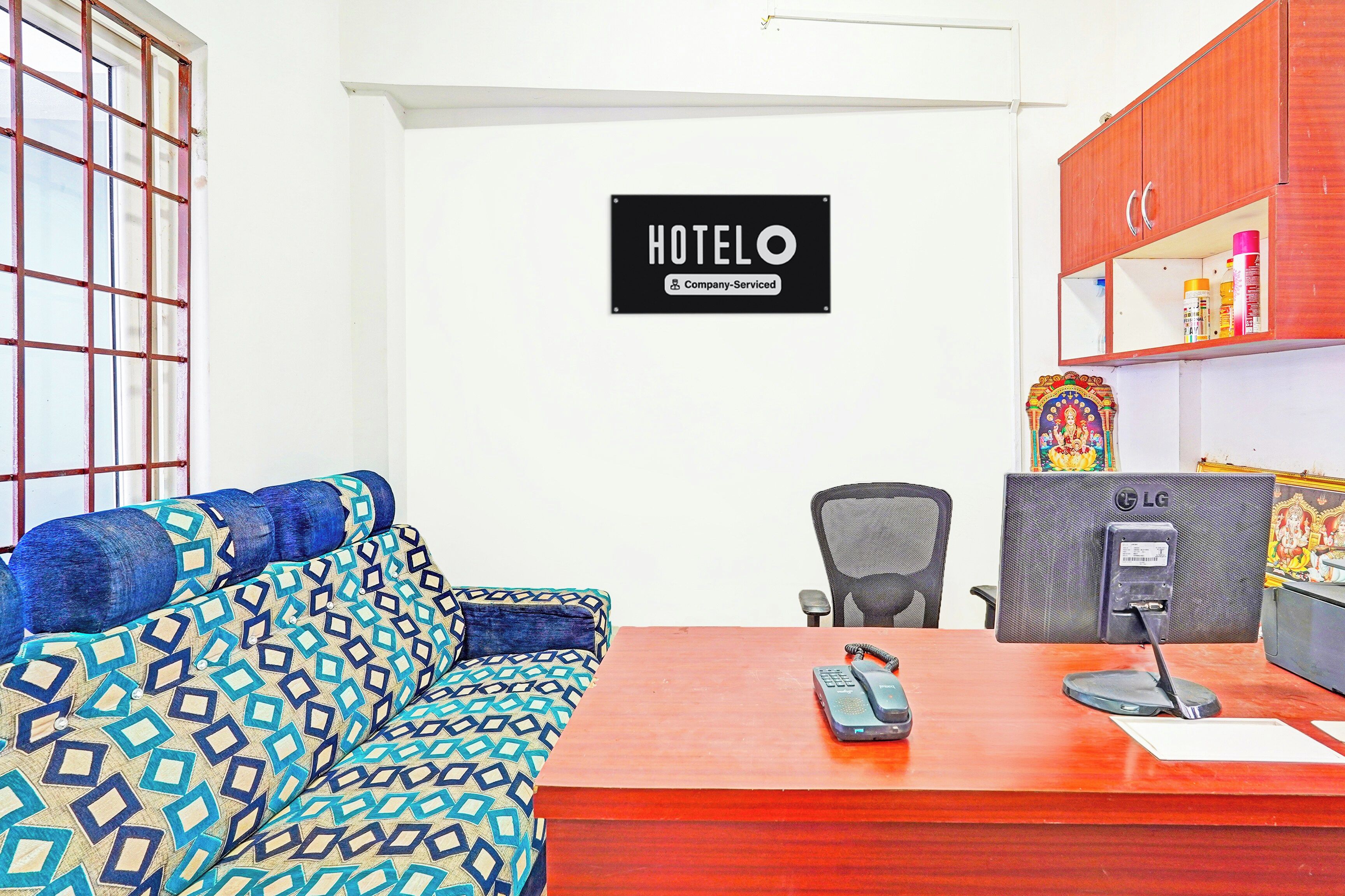 Une chambre d’hôtel équipée d’un canapé, d’un bureau avec un téléphone, d’une chaise et d’une enseigne fixée au mur indiquant « Hôtel – Services proposés par la société ».