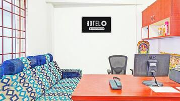 Une chambre d’hôtel équipée d’un canapé, d’un bureau avec un téléphone, d’une chaise et d’une enseigne fixée au mur indiquant « Hôtel – Services proposés par la société ».