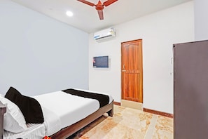 A bedroom with a bed, a wooden door, a television, and a ceiling fan. - Hotel O Sholinganallur Near Anjaneya (Chennai)