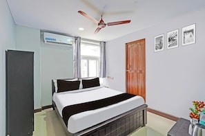 A hotel room with a bed, a ceiling fan, a window with curtains, a wooden door, and framed pictures on the wall. - Hotel O Sholinganallur Near Anjaneya (Chennai)