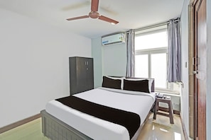A hotel room with a bed, a wardrobe, a ceiling fan, an air conditioning unit, a window with curtains, and a small stool. - Hotel O Sholinganallur Near Anjaneya (Chennai)