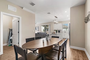 A modern kitchen with white cabinets, a central island, and a dining area with a round table and chairs. - NEW Family Reunion Epic Game Room Resort Pool 7837 (Kissimmee)