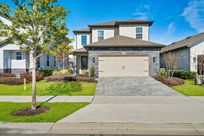 A two-story residential house with a stone facade, a garage, and a well-maintained lawn. - NEW Family Reunion Epic Game Room Resort Pool 7837 (Kissimmee)