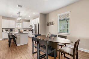 A modern kitchen with white cabinets, a central island, and a dining area with a round table and chairs. - NEW Family Reunion Epic Game Room Resort Pool 7837 (Kissimmee)
