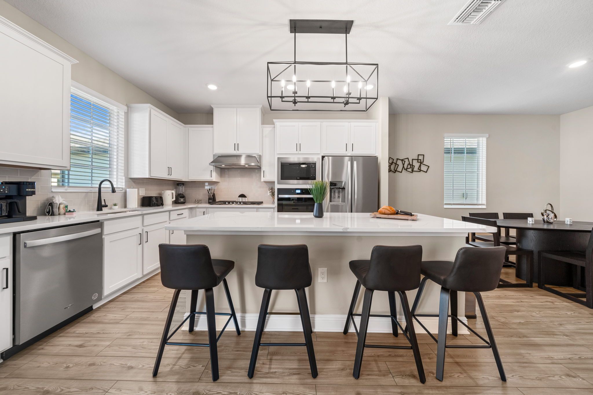 A modern kitchen with white cabinetry, stainless steel appliances, and a central island with bar stools.