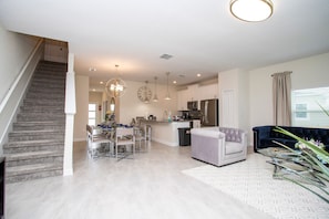 A spacious living area with a staircase, a dining table with chairs, a sofa, and a kitchen with modern appliances. - NEW 5BR Private Pool Lazy River Resort 8955 (Davenport)