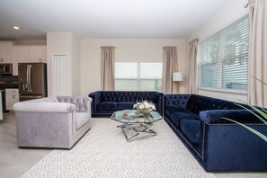 A modern living room with a grey sofa, a blue sofa, and a white armchair. There is a glass coffee table with a flower vase. - NEW 5BR Private Pool Lazy River Resort 8955 (Davenport)