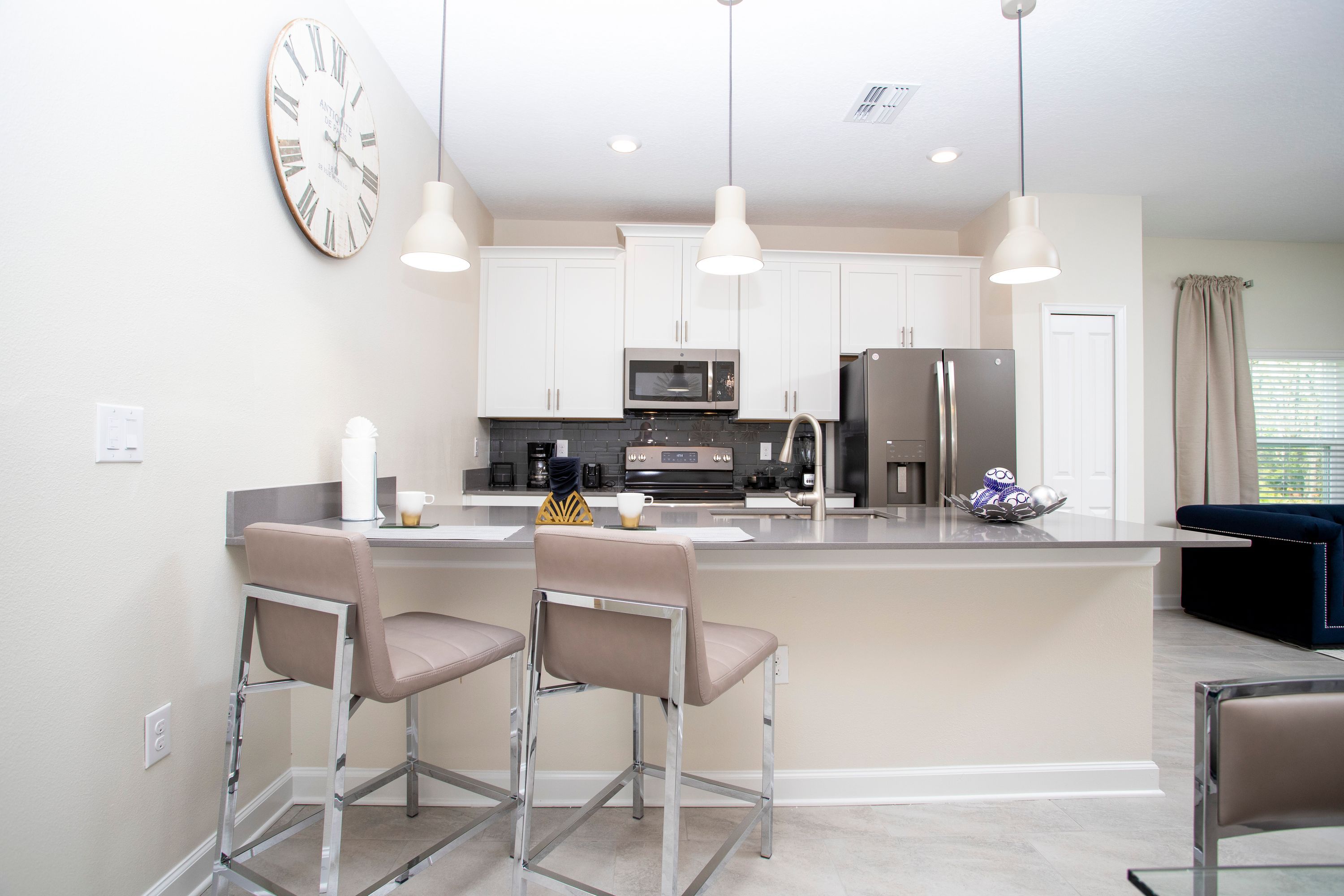 A modern kitchen with a central island, bar stools, stainless steel appliances, and pendant lighting.
