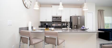 A modern kitchen with a central island, bar stools, stainless steel appliances, and pendant lighting.